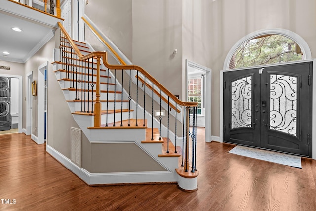 entrance foyer with wood finished floors, a high ceiling, stairway, baseboards, and ornamental molding