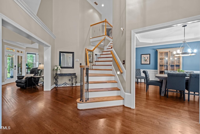 stairway with french doors, wood finished floors, a chandelier, ornamental molding, and baseboards