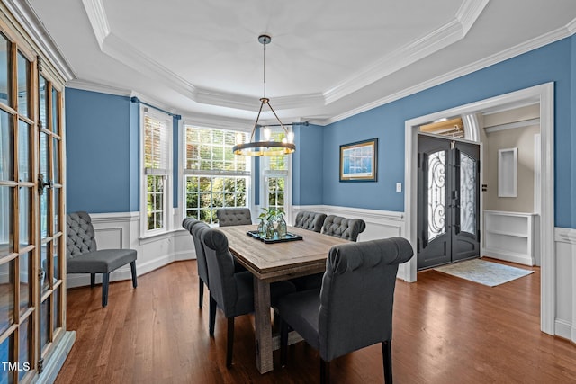dining area featuring french doors, wood finished floors, a raised ceiling, a chandelier, and wainscoting