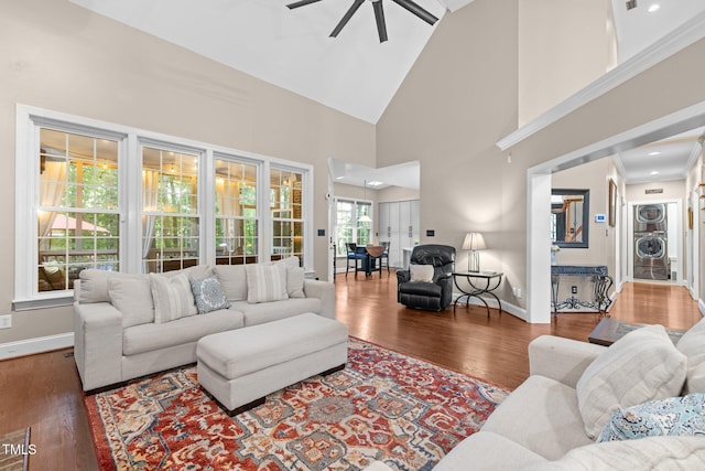 living area featuring ceiling fan, stacked washer / drying machine, wood finished floors, baseboards, and high vaulted ceiling