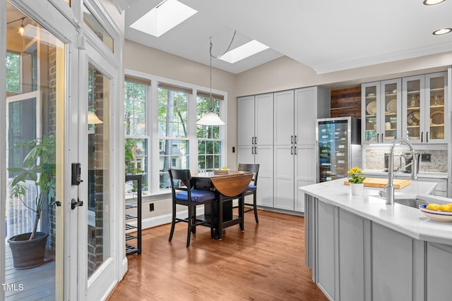 kitchen with a skylight, a sink, wine cooler, pendant lighting, and glass insert cabinets