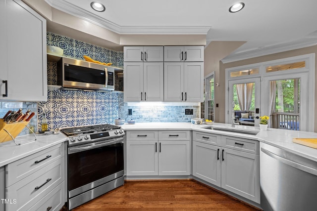 kitchen with appliances with stainless steel finishes, crown molding, light countertops, decorative backsplash, and a sink