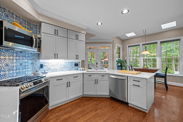 kitchen featuring stainless steel appliances, a skylight, a peninsula, light countertops, and wood finished floors