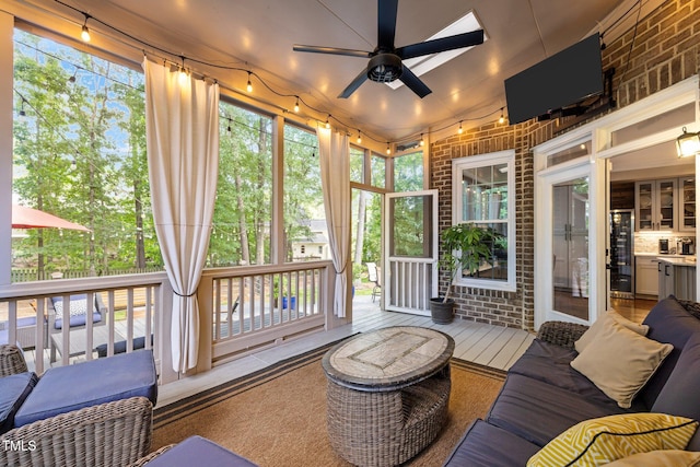 sunroom with brick wall, ceiling fan, and a wooden deck