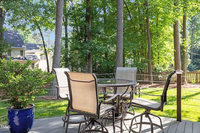 deck featuring fence, outdoor dining space, and view of wooded area