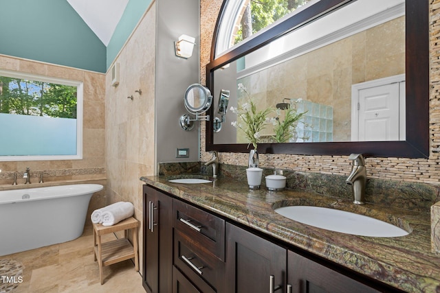 bathroom with double vanity, tile walls, a freestanding tub, vaulted ceiling, and backsplash