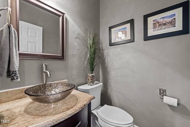 half bathroom with a textured wall, toilet, and vanity