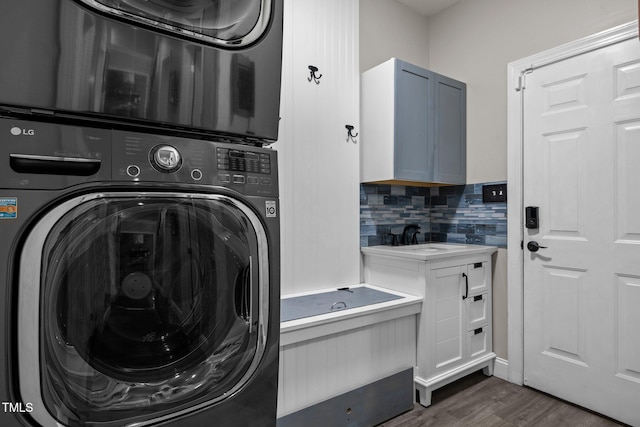 clothes washing area featuring stacked washer / drying machine, dark wood-style flooring, and cabinet space