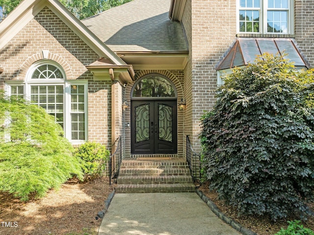 view of exterior entry with brick siding, a shingled roof, and french doors