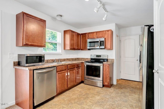 kitchen with track lighting, a sink, appliances with stainless steel finishes, and brown cabinets