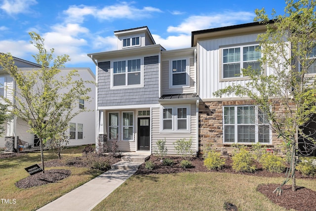 view of front of house with board and batten siding, stone siding, and a front yard
