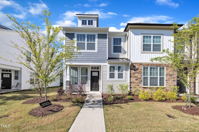 townhome / multi-family property with board and batten siding, a front yard, and stone siding