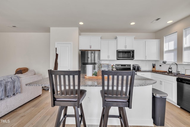 kitchen featuring a breakfast bar area, appliances with stainless steel finishes, a sink, light wood-style floors, and white cabinetry