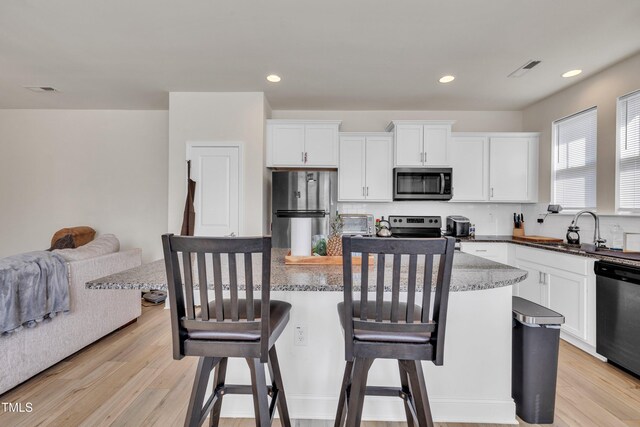 162 Channel Drop Dr, Clayton, NC 27520 - kitchen featuring a breakfast bar area, appliances with stainless steel finishes, a sink, light wood-style floors, and white cabinetry