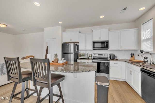 kitchen with visible vents, a kitchen breakfast bar, a sink, light wood-style flooring, and appliances with stainless steel finishes