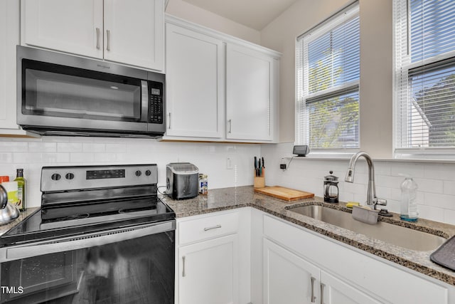 kitchen with white cabinets, tasteful backsplash, a sink, dark stone countertops, and appliances with stainless steel finishes