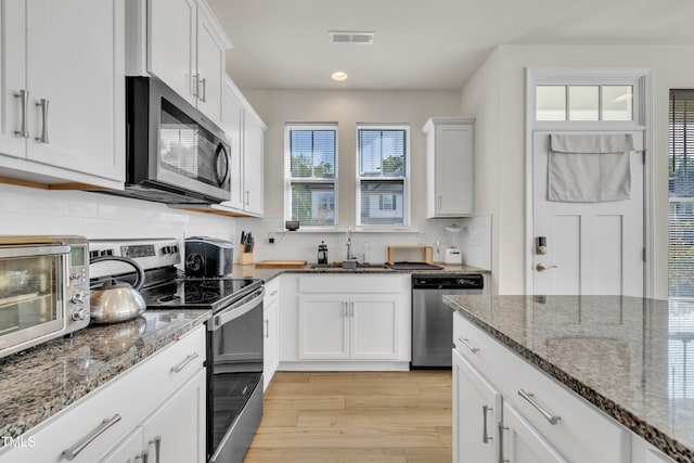 kitchen with a sink, white cabinets, light wood-style floors, dark stone counters, and stainless steel appliances