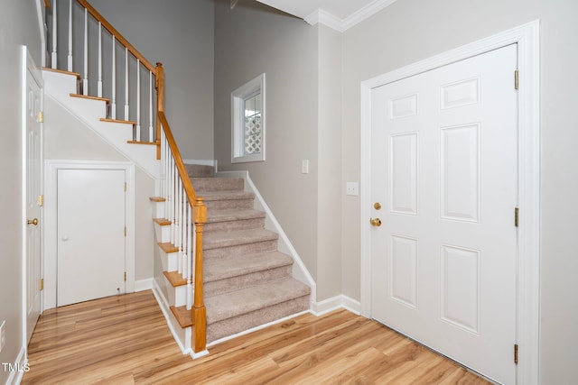 entryway with light wood-style floors, stairs, crown molding, and baseboards