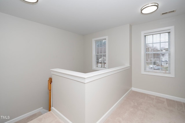 hallway with carpet floors, baseboards, an upstairs landing, and visible vents