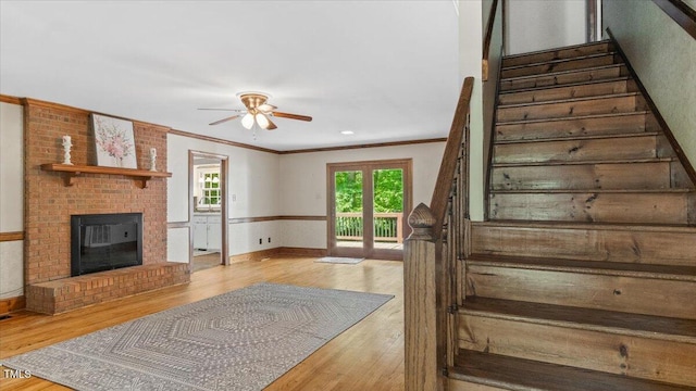 stairway featuring wood finished floors, a ceiling fan, a fireplace, crown molding, and baseboards