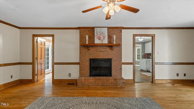 unfurnished living room with ornamental molding, wainscoting, ceiling fan, and wood finished floors