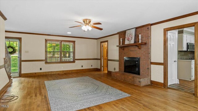 unfurnished living room featuring wood finished floors, a ceiling fan, a fireplace, baseboards, and ornamental molding