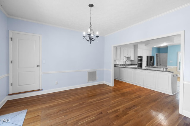 unfurnished dining area with a chandelier, dark wood-type flooring, crown molding, baseboards, and a sink