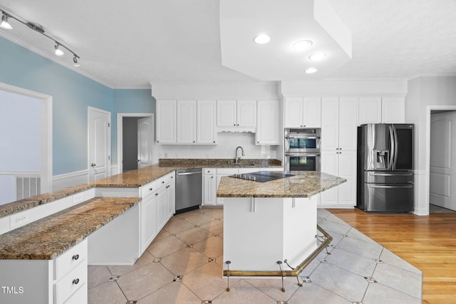 kitchen with stainless steel appliances, a peninsula, a sink, white cabinets, and dark stone countertops