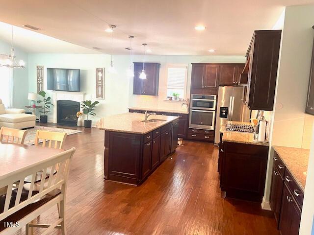kitchen with hanging light fixtures, open floor plan, light stone counters, and a sink