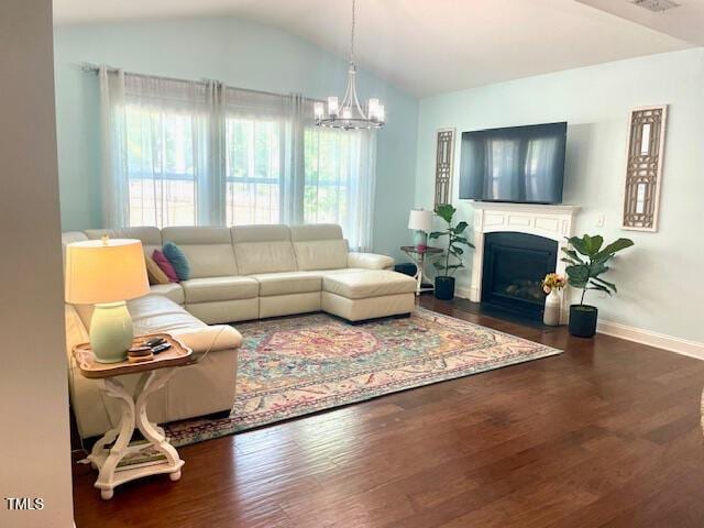 living area with wood finished floors, baseboards, a fireplace with flush hearth, a notable chandelier, and vaulted ceiling
