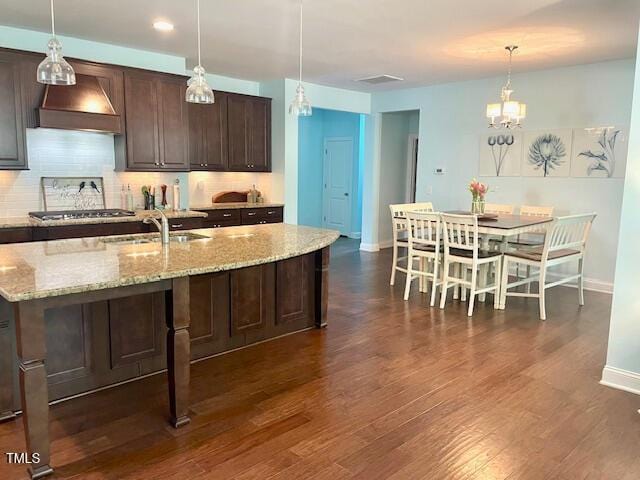 kitchen with stainless steel gas stovetop, wall chimney range hood, backsplash, and a sink