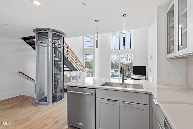kitchen featuring a sink, stainless steel dishwasher, a peninsula, light wood-style flooring, and glass insert cabinets