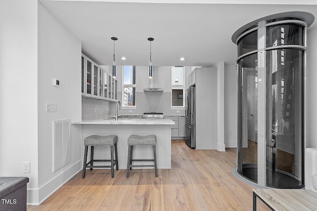 kitchen featuring wall chimney exhaust hood, stainless steel fridge, a peninsula, a breakfast bar area, and light wood-type flooring