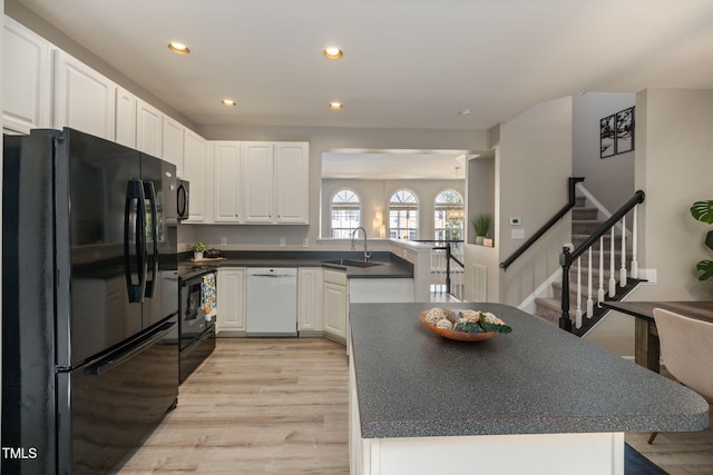 kitchen featuring light wood-type flooring, a sink, black appliances, and dark countertops