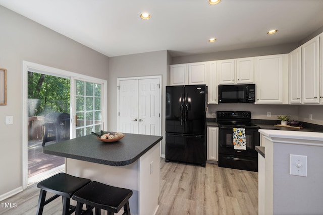 kitchen with white cabinets, dark countertops, a breakfast bar, light wood finished floors, and black appliances