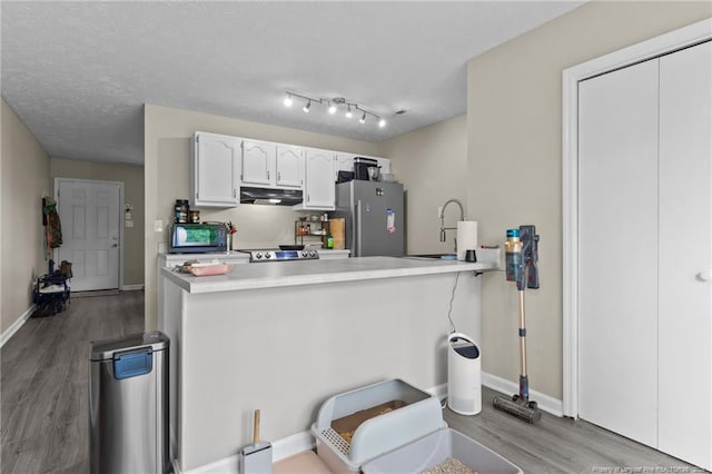 kitchen with freestanding refrigerator, a peninsula, wood finished floors, range hood, and white cabinets