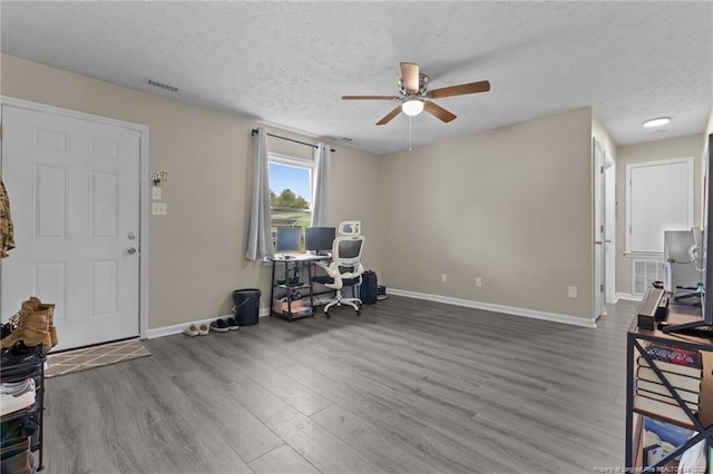 office space featuring ceiling fan, a textured ceiling, baseboards, wood finished floors, and visible vents