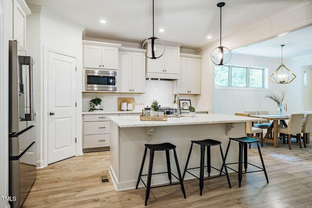 151 Monteith Dr, Chapel Hill, NC 27516 - kitchen featuring appliances with stainless steel finishes, ornamental molding, light wood-style flooring, white cabinetry, and a kitchen bar