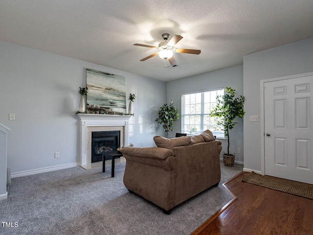 living area featuring ceiling fan, a glass covered fireplace, baseboards, wood finished floors, and a textured ceiling
