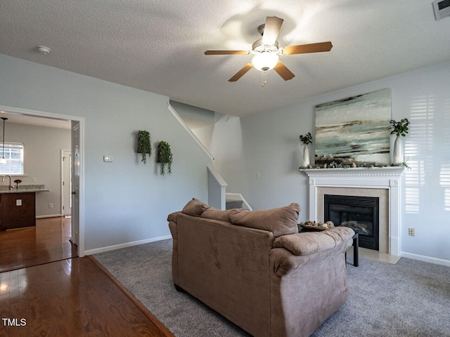 living area with ceiling fan, stairway, a fireplace with flush hearth, wood finished floors, and baseboards