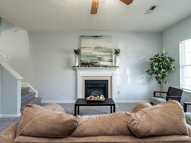 carpeted living area featuring ceiling fan, stairway, a textured ceiling, a glass covered fireplace, and baseboards