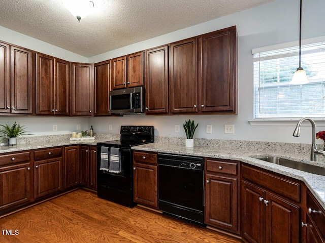 kitchen with black appliances, a sink, wood finished floors, a textured ceiling, and light stone countertops