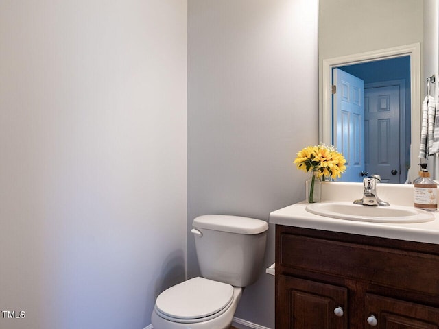 half bathroom featuring baseboards, toilet, and vanity