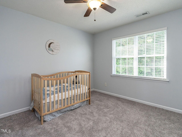 bedroom featuring carpet, a crib, baseboards, a textured ceiling, and a ceiling fan