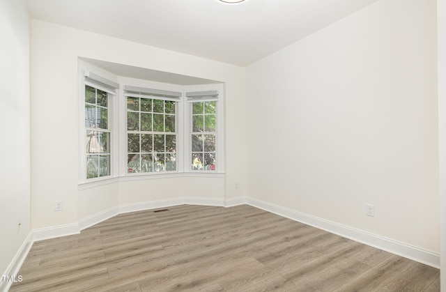unfurnished room with baseboards, light wood-style flooring, and a wealth of natural light