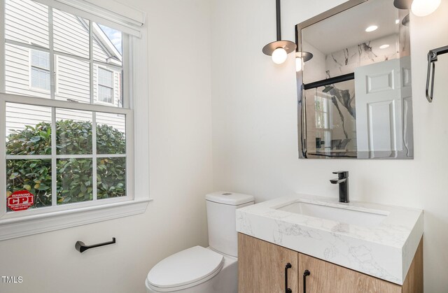 full bath with toilet, a marble finish shower, and vanity