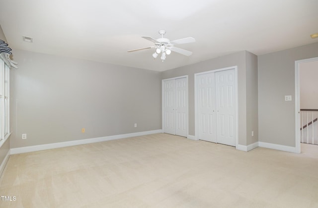 unfurnished bedroom with light colored carpet, multiple closets, and visible vents