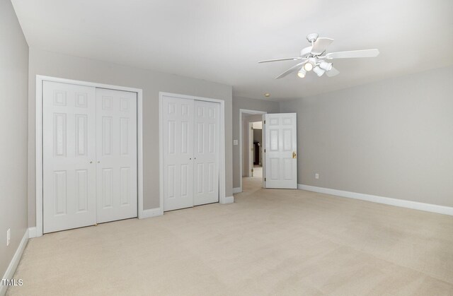 unfurnished bedroom featuring baseboards, two closets, and light carpet
