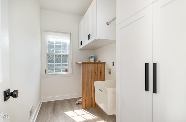 interior space featuring visible vents, baseboards, hookup for a washing machine, light wood-type flooring, and cabinet space