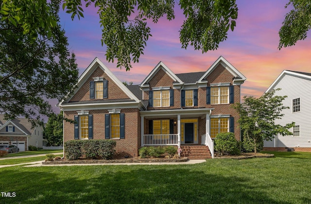view of front of home featuring covered porch, brick siding, and a lawn